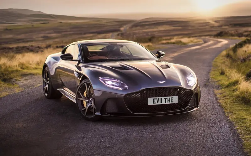 Grey Aston Martin on a moorland road at sunset wearing the registration EV11 THE