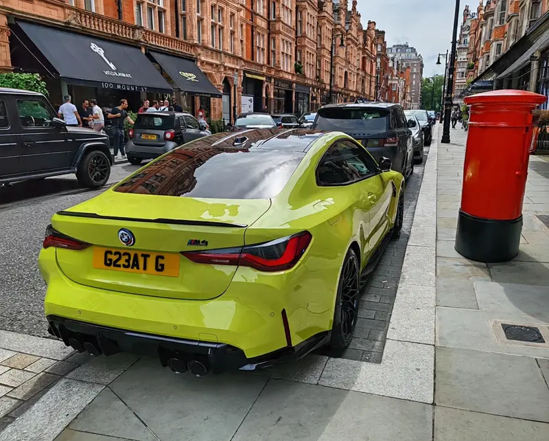 Yellow BMW M4 parked on a London street beside a red pillar box, wearing the registration G23 ATG